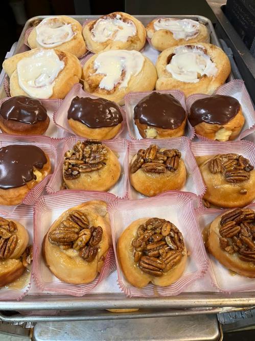 A tray of assorted pastries, including cinnamon rolls with icing and chocolate-covered treats topped with pecans.