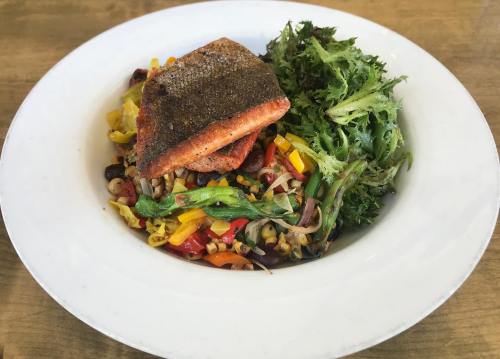 A plate of grilled salmon atop a colorful vegetable and grain salad, accompanied by a side of mixed greens.