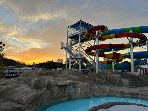 A water park at sunset featuring colorful water slides and a rocky landscape with a pool in the foreground.