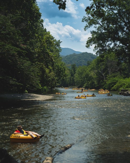 A serene river scene with people floating on yellow inner tubes surrounded by lush greenery and mountains in the background.