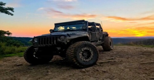 A rugged off-road vehicle parked on a dirt path, with a vibrant sunset in the background.
