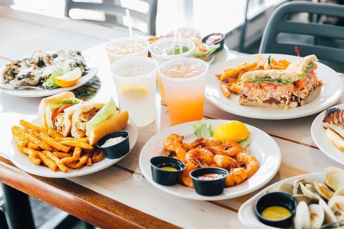 A table filled with various dishes, including shrimp, sandwiches, fries, and drinks in a casual dining setting.