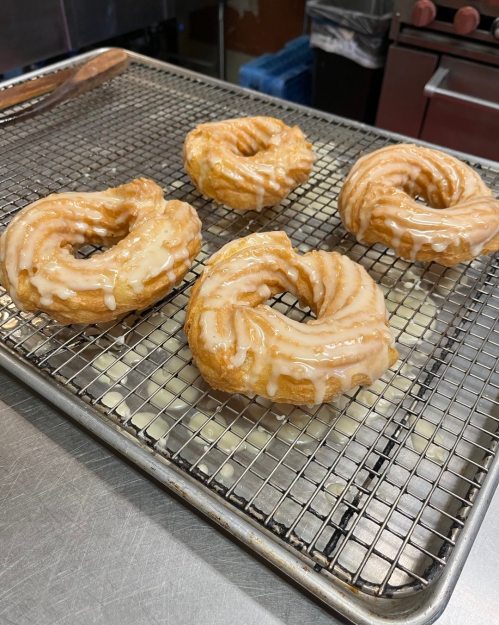 Four glazed donuts on a wire rack, with a shiny icing coating, resting on a stainless steel surface.