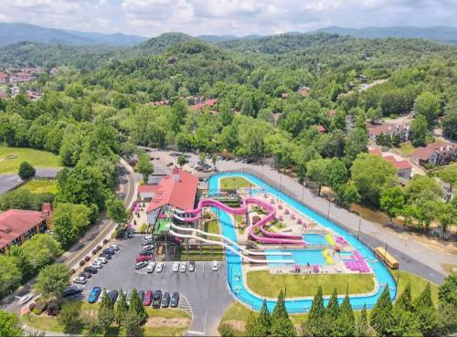 Aerial view of a water park with colorful slides, a lazy river, and surrounding green hills and trees.