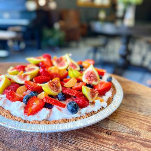 A colorful fruit tart topped with strawberries, figs, blueberries, and citrus on a wooden table.