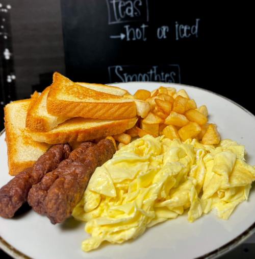 A plate of breakfast featuring scrambled eggs, sausage links, toast, and golden potato cubes.