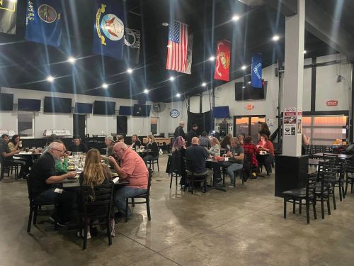 A spacious dining area with people eating at tables, flags hanging from the ceiling, and a casual atmosphere.