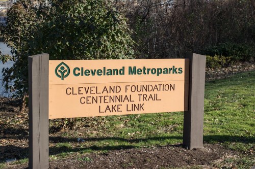 Sign for Cleveland Metroparks featuring "Cleveland Foundation Centennial Trail" and "Lake Link" with greenery in the background.