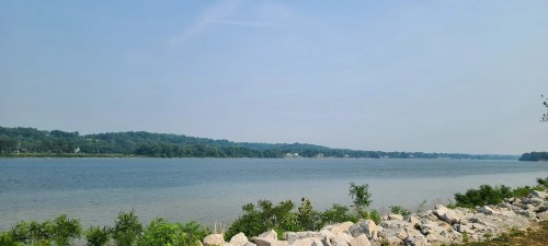 A calm river scene with rocky shorelines and lush green hills under a clear blue sky.