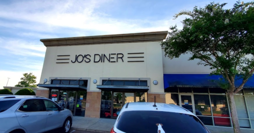 Exterior of Jo's Diner, featuring a large sign and parked cars in front under a clear blue sky.