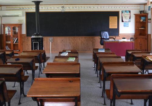 A classroom with wooden desks, a blackboard, a teacher's desk, and a wood stove in a cozy, inviting setting.