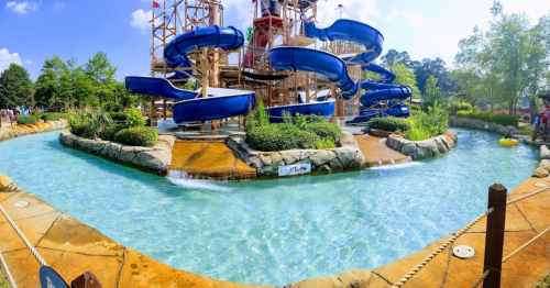 A water park featuring blue slides, a lazy river, and lush greenery under a bright blue sky.