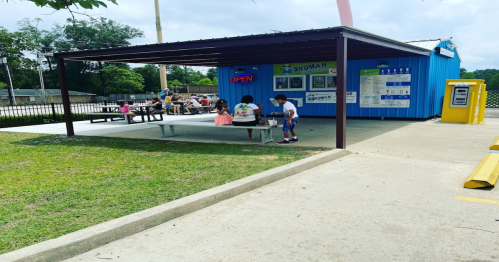 A blue building with an open sign, featuring people enjoying snacks under a covered area and picnic tables outside.