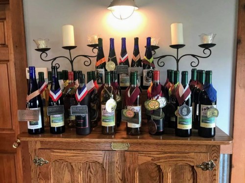 A display of various wine bottles adorned with medals and ribbons, arranged on a wooden cabinet.