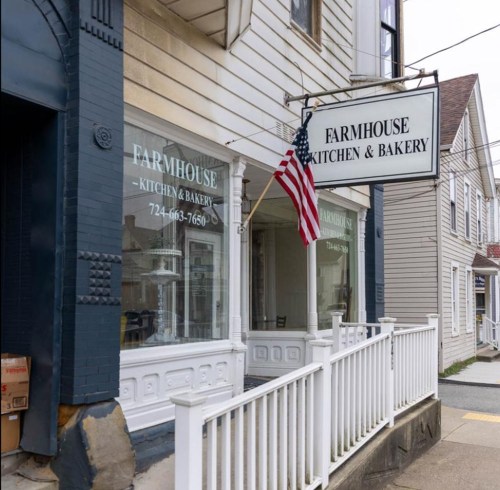 Exterior of Farmhouse Kitchen & Bakery, featuring a sign and an American flag, with a white railing in front.