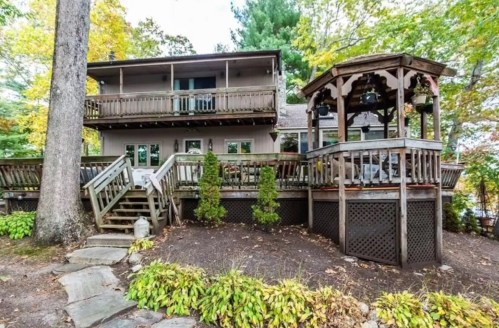 A two-story house with a wooden deck and gazebo, surrounded by trees and landscaped greenery.