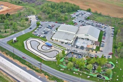 Aerial view of a recreational facility with go-kart track, mini-golf, and a large parking lot surrounded by greenery.