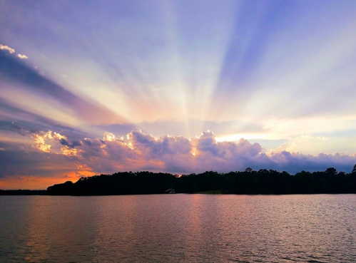 A serene sunset over a calm lake, with vibrant rays of light breaking through colorful clouds.