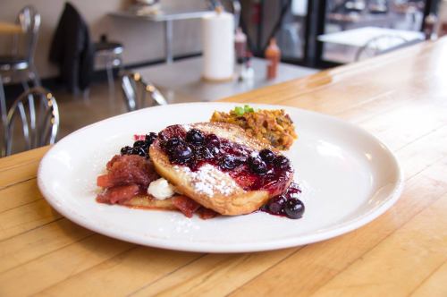 A plate of French toast topped with berries and powdered sugar, served with a side of savory dish.
