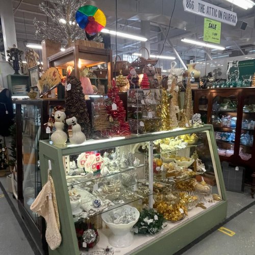 A display case filled with festive decorations, including snowmen, gold accents, and colorful ornaments in a vintage shop.