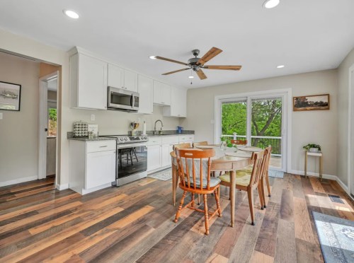 Bright kitchen with wooden floors, a round dining table, and sliding doors leading to a green outdoor view.