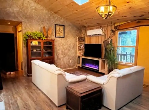 Cozy living room with a white sectional sofa, wooden accents, a TV, and a warm atmosphere from natural light.