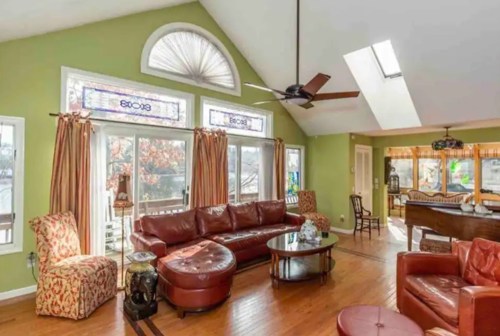 Bright living room with green walls, large windows, a leather sofa, and a wooden dining area.