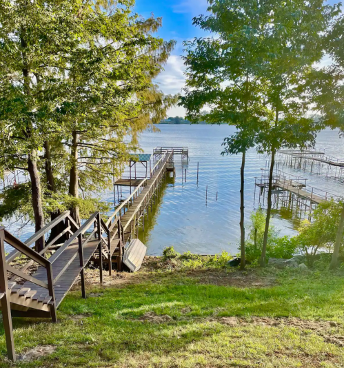 A serene lakeside view with wooden docks, surrounded by trees and a clear blue sky.