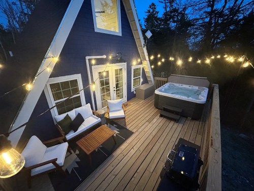 Cozy deck with a hot tub, string lights, and seating area, surrounded by trees at dusk.