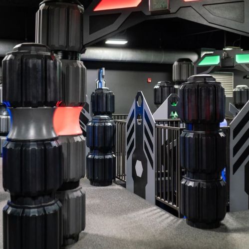 A colorful indoor laser tag arena featuring black pillars and geometric structures for players to hide behind.