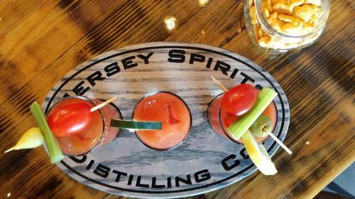 Three colorful cocktails with garnishes on a wooden tray, alongside a jar of snacks.