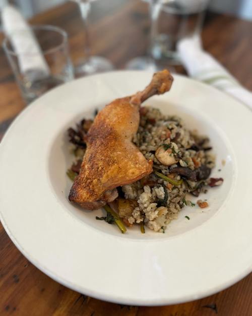 A plate of seasoned rice with vegetables topped by a crispy chicken leg, served on a wooden table.
