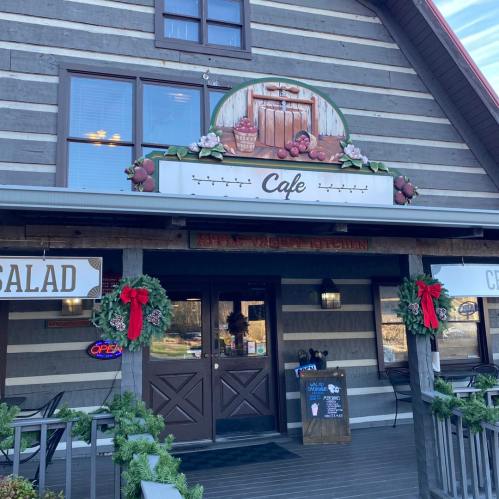 A rustic cafe with a wooden facade, festive wreaths, and a sign reading "Cafe" above the entrance.
