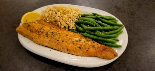 A plate with a golden-brown fish fillet, brown rice, and green beans, garnished with a lemon wedge.