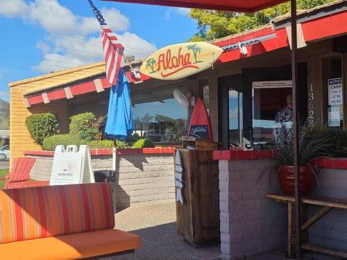 A colorful restaurant exterior with a surfboard sign, flags, and outdoor seating under a blue sky.