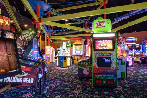 A vibrant arcade filled with colorful game machines and neon decor, featuring various games and bright lighting.