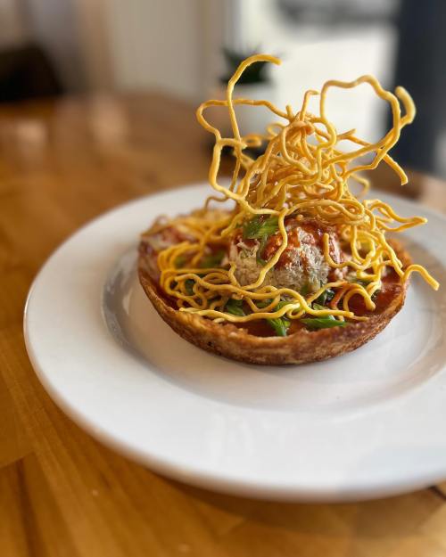 A crispy bowl filled with noodles, topped with a meatball and garnished with fried noodles and green onions.