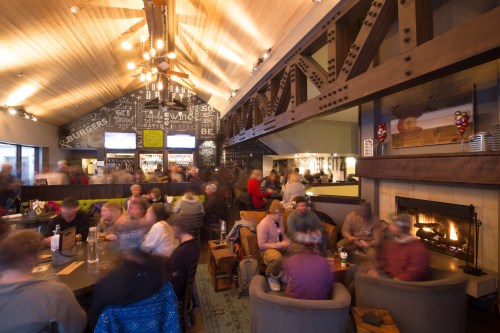 A bustling restaurant interior with patrons enjoying food and drinks, a fireplace, and a cozy atmosphere.