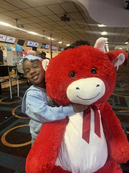 A smiling child hugs a large red stuffed animal in a bowling alley.