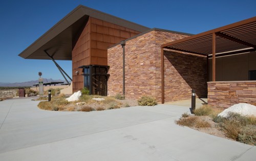 Modern building with a copper roof and stone facade, surrounded by desert landscaping and clear blue skies.