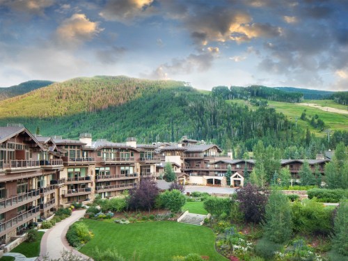 Scenic view of a resort nestled in lush green mountains under a dramatic sky, featuring landscaped gardens and buildings.