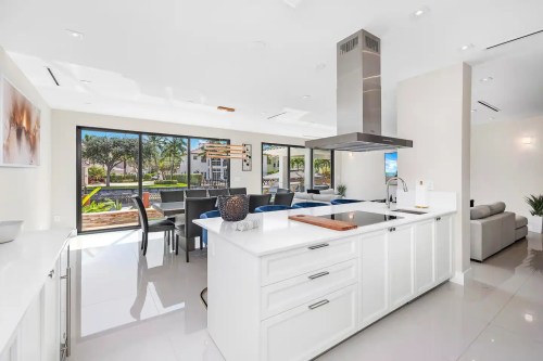 Modern kitchen with white cabinetry, island, and large windows overlooking a patio and greenery. Bright and airy space.