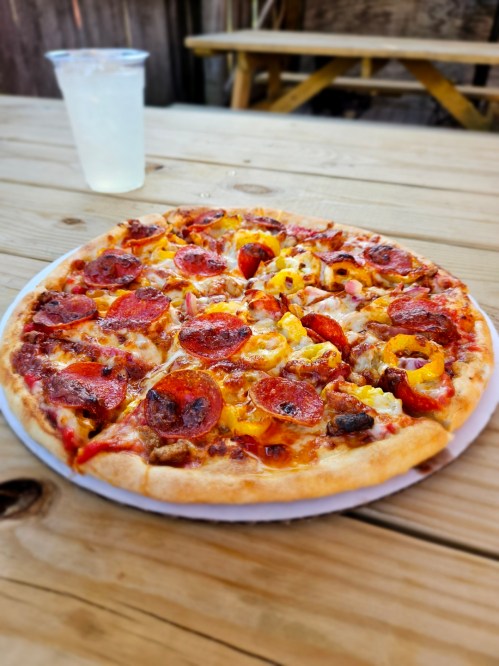 A delicious pepperoni pizza topped with cheese and pineapple, served on a wooden table with a drink in the background.