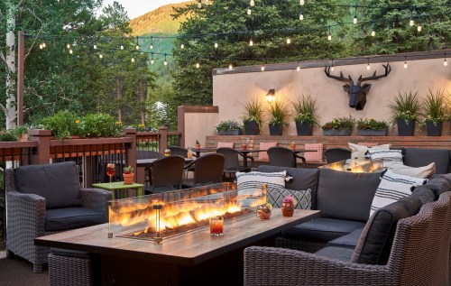 Cozy outdoor patio with a fire table, comfortable seating, and string lights, surrounded by greenery and mountain views.