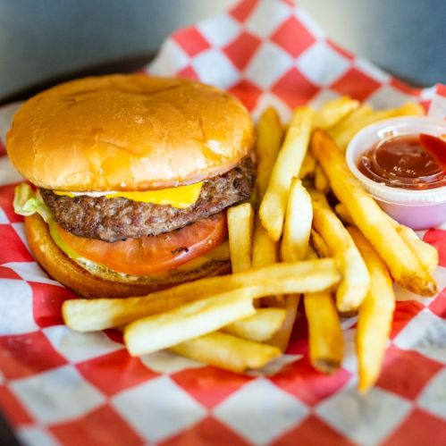 A cheeseburger with lettuce, tomato, and fries on a red and white checkered plate, accompanied by a small cup of ketchup.