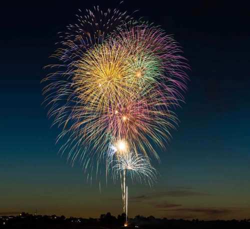 Colorful fireworks burst in the night sky, illuminating the dark with vibrant hues of pink, green, and gold.