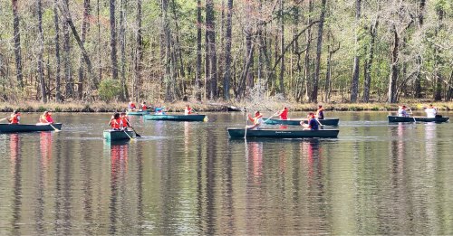 A group of people in canoes paddling on a calm lake surrounded by trees.