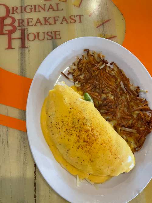 A plate featuring a cheese omelet with a side of crispy hash browns on a table with "Original Breakfast House" logo.