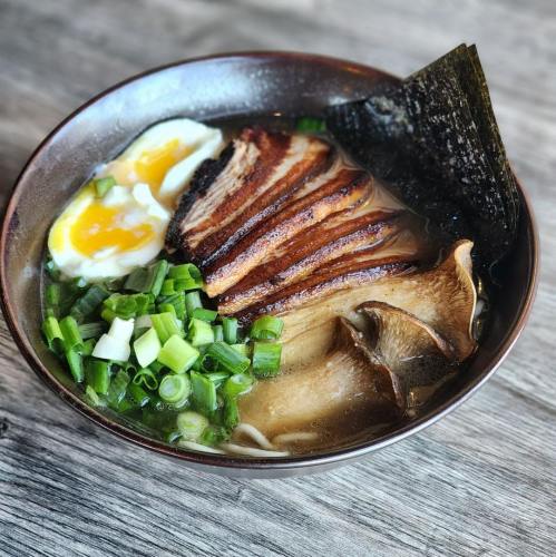 A bowl of ramen with sliced pork, soft-boiled egg, green onions, and seaweed on a wooden surface.