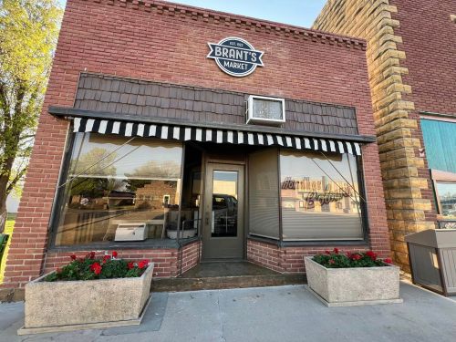 Exterior of Brant's Market, a brick building with large windows and flower planters, featuring a striped awning.